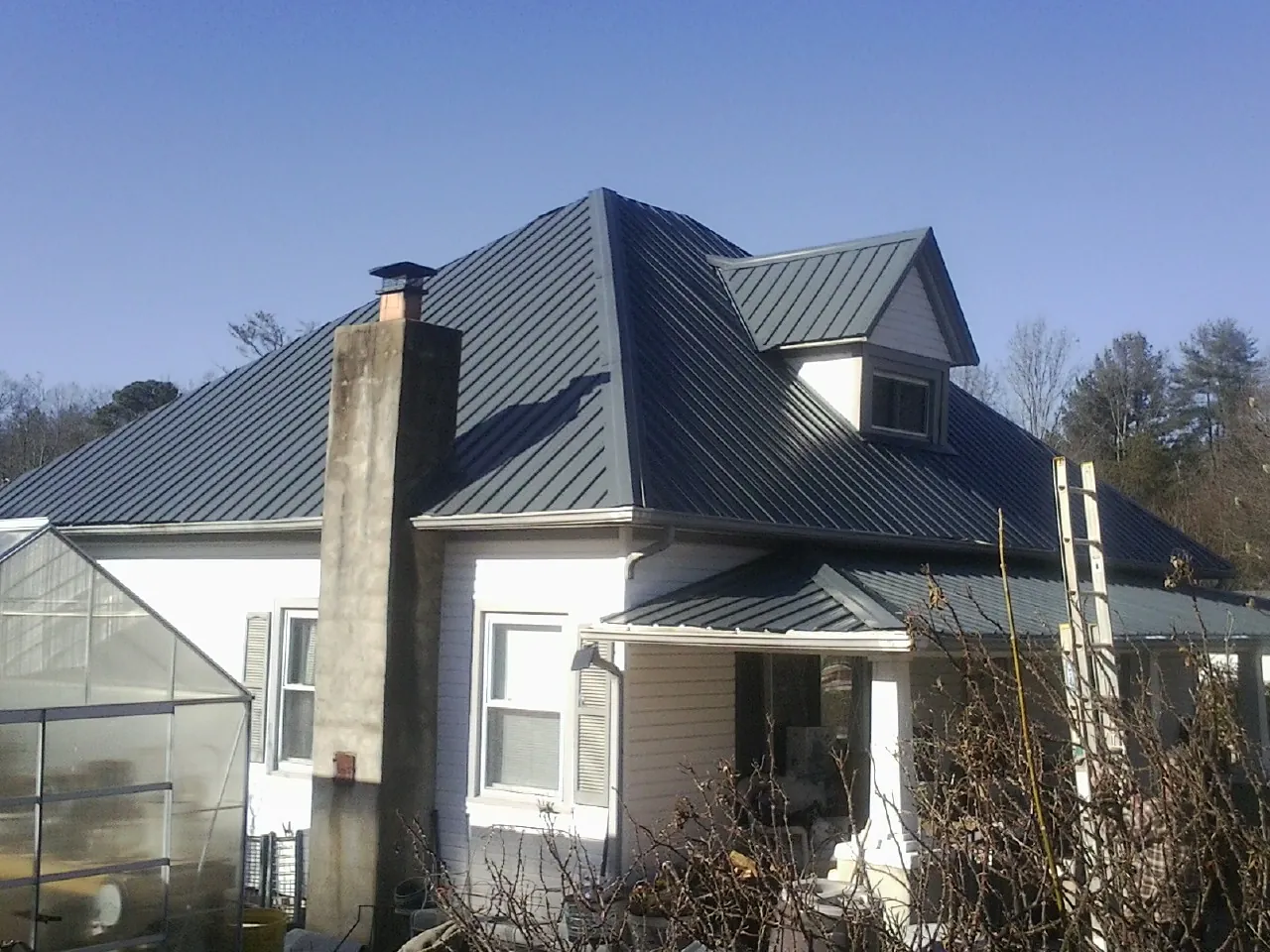 Dark blue standing seam metal roof on a white farmhouse with dormer — Slate & Tile Roof Repair by Roofing Brothers in Fruitport