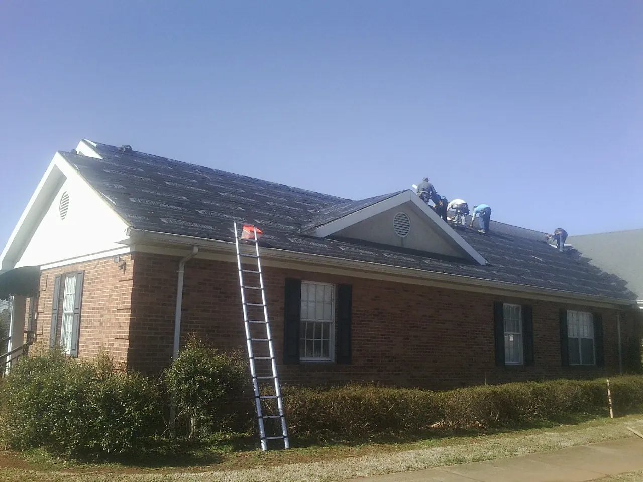 Crew tearing shingles off a brick ranch roof with a ladder set — Metal Roof Repair work by our crew in Fruitport