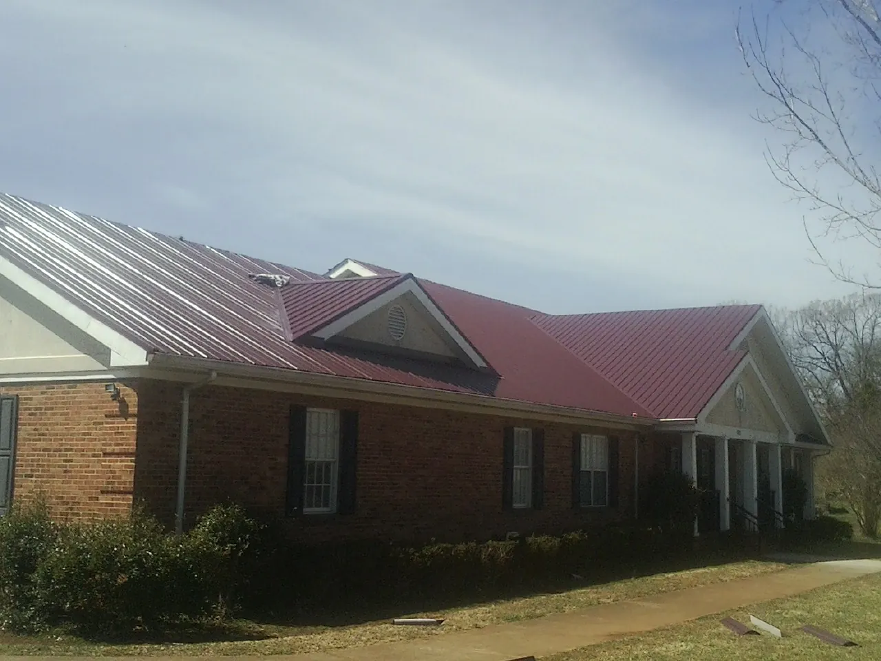 Red metal roof with gabled entries on a long brick building, from a Hail Damage Roof Repair job in Fruitport