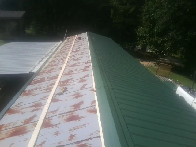 Old rusted panels beside newly installed green metal roofing — Wind Damage Roof Repair by Roofing Brothers in Fruitport