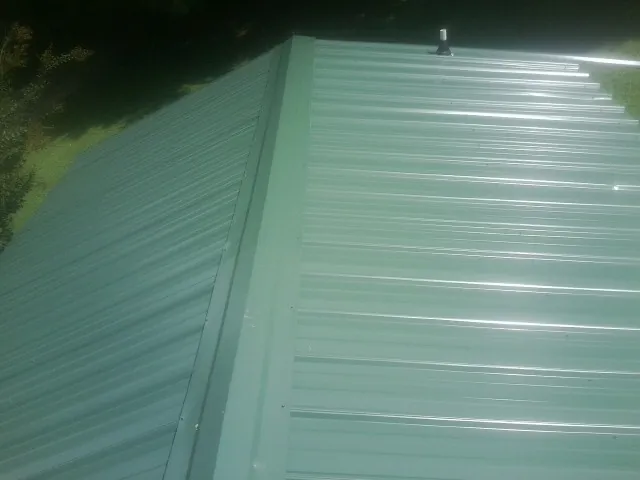 New green metal panels meeting at the ridge of a roof — Flat Roof Repair work by our crew in Fruitport