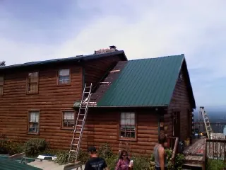 Green metal roof going on a two story log home with ladders set in Fruitport