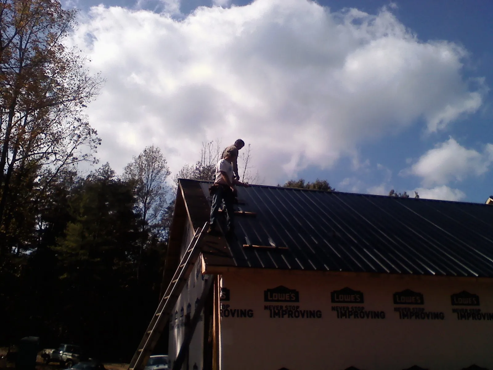 Roofer fastening dark metal panels high against a cloudy sky, from a Roof Inspection job in Fruitport
