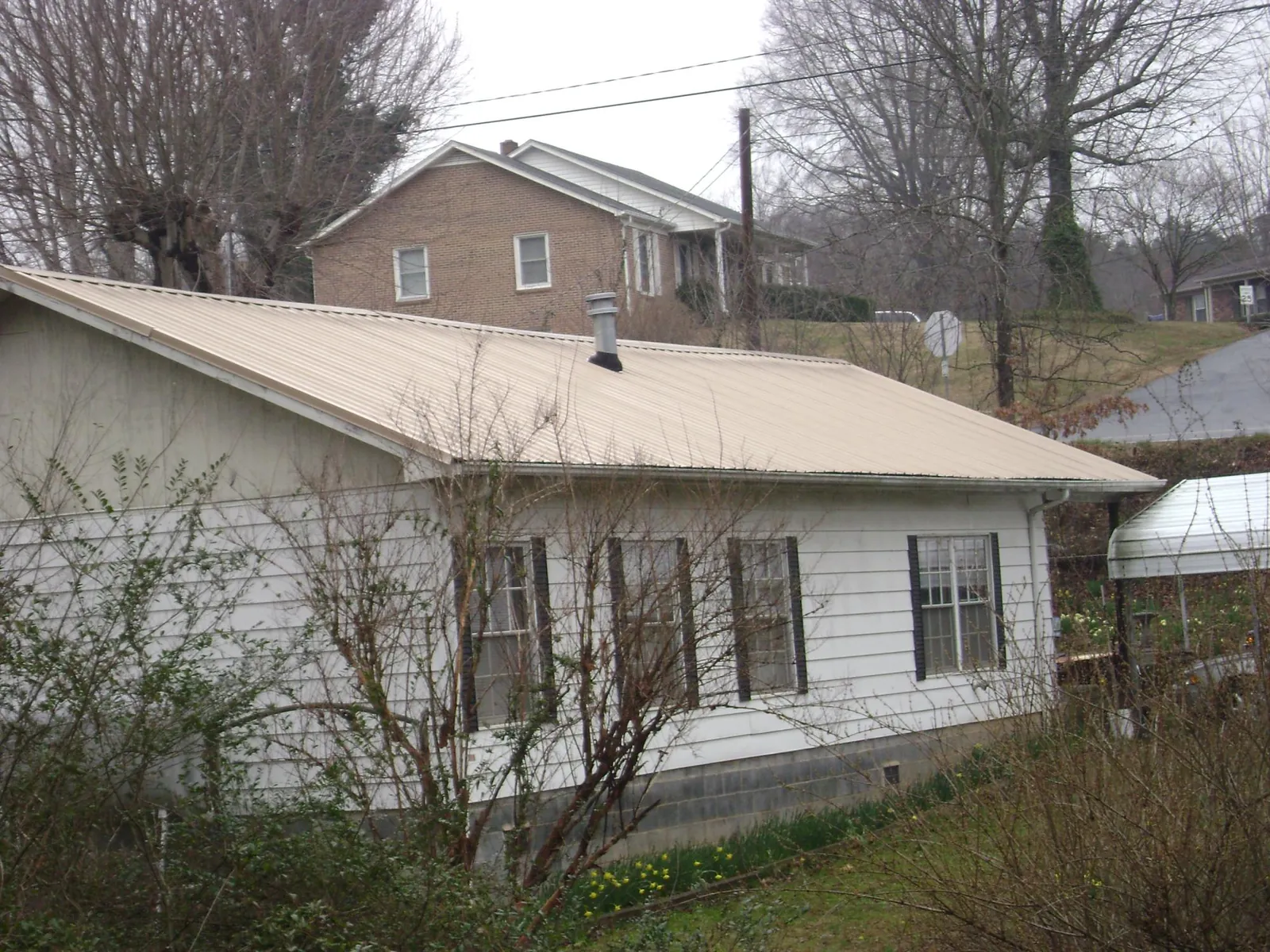 Tan metal roof on a white sided house set into a hillside — Commercial Roofing by Roofing Brothers in Fruitport